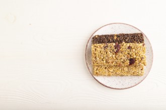 Granola bars with caramel, nuts, flakes in ceramic plate on white wooden background. Top view, flat