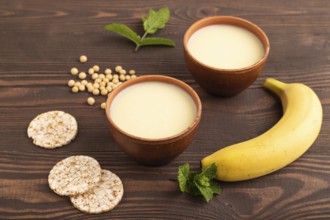 Organic non dairy banana and soy milk in clay cup on brown wooden background. Vegan healthy food