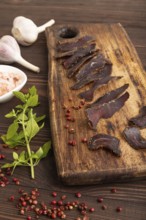 Armenian Basturma dried meat on wooden cutting board with pepper and herbs on brown wooden