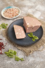 Mortadella sausage on plate with pepper and herbs on brown concrete background and linen textile.