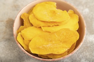 Dried Mango in ceramic bowl on brown concrete background. Side view, close up, selective focus.