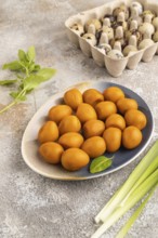 Pile of Smoked Quail eggs on plate on a brown concrete background. side view, close up