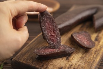 Sujuk sausage with hand on wooden cutting board with pepper and herbs on brown wooden background.
