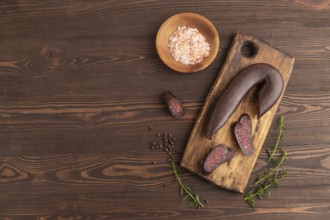 Sujuk sausage on wooden cutting board with pepper and herbs on brown wooden background. Top view,