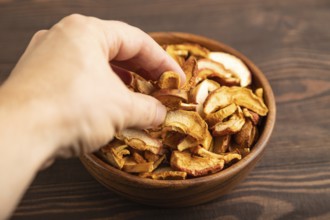 Dried Apples in wooden bowl with hand on brown wooden background. Side view, close up, healthy
