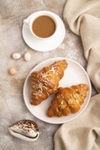 Croissant on white plate on brown concrete background and linen textile, cup of coffee, top view,