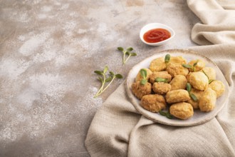 Fried crispy Chicken Nuggets with ketchup, microgreen on brown concrete background and linen