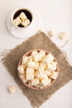 Orange and pink marshmallow in ceramic bowl on white wooden background and linen textile, top view,