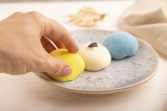 Japanese Mochi Cakes with hand on white wooden background and linen textile, side view, close up,