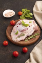 Raw Turkey Thigh with spices and rosemary on cutting board on black concrete background and linen