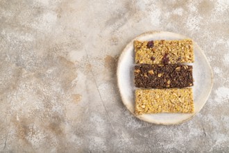 Granola bars with caramel, nuts, flakes in ceramic plate on brown concrete background. Top view,