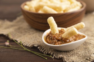 Corn flakes sticks with caramel in wooden bowl on brown wooden background and linen textile. Side