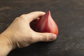 Red Heart shape tomatoes with hand on black concrete background. Side view, copy space. healthy