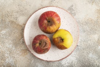 Decaying, Rotting apples on ceramic plate on brown concrete background. Top view, copy space, flat