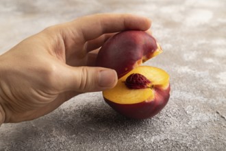 Peach Cut in half with hand on brown concrete background. Side view, copy space. healthy food,
