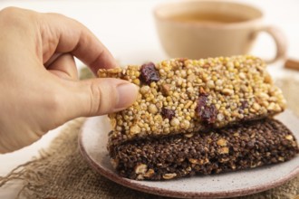 Granola bars with caramel, nuts, flakes in ceramic plate with hand on white wooden background,