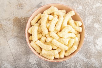 Corn flakes sticks with caramel in ceramic bowl on gray concrete background. Top view, flat lay,