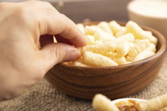 Corn flakes sticks with caramel in wooden bowl with hand on brown wooden background and linen