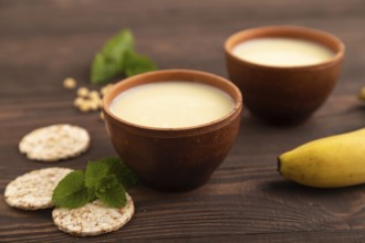 Organic non dairy banana and soy milk in clay cup on brown wooden background. Vegan healthy food