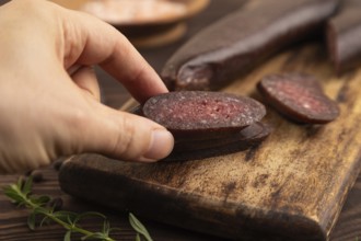 Sujuk sausage with hand on wooden cutting board with pepper and herbs on brown wooden background.