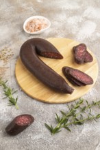 Sujuk sausage on wooden cutting board with pepper and herbs on brown concrete background. Side