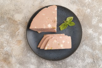 Mortadella sausage on plate with pepper and herbs on brown concrete background. Top view, flat lay,