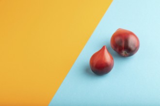 Red Heart shape tomatoes on blue and orange pastel paper background. Side view, copy space. healthy