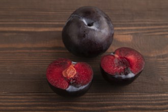 Purple Plum Cut in half on brown wooden background. Side view, close up. healthy food, vegetable,