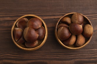 Wooden bowl with raw edible ?hestnuts on brown wooden background, top view, flat lay, close up,
