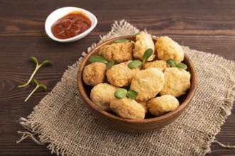 Fried crispy Chicken Nuggets with ketchup, microgreen on brown wooden background and linen textile.