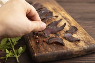 Armenian Basturma dried meat with hand on wooden cutting board with pepper and herbs on brown
