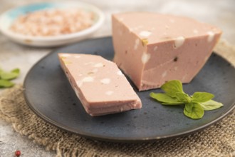 Mortadella sausage on plate with pepper and herbs on brown concrete background and linen textile.