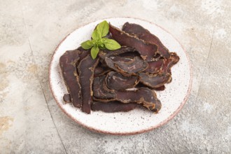 Armenian Basturma dried meat on plate with pepper and herbs on brown concrete background. Side