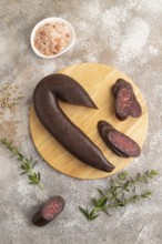 Sujuk sausage on wooden cutting board with pepper and herbs on brown concrete background. Top view,