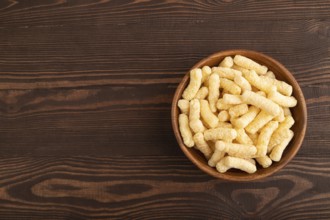 Corn flakes sticks with caramel in wooden bowl on brown wooden background. Top view, flat lay, copy