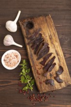 Armenian Basturma dried meat on wooden cutting board with pepper and herbs on brown wooden