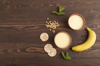 Organic non dairy banana and soy milk in clay cup on brown wooden background. Vegan healthy food