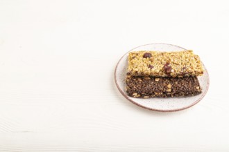 Granola bars with caramel, nuts, flakes in ceramic plate on white wooden background. Side view,