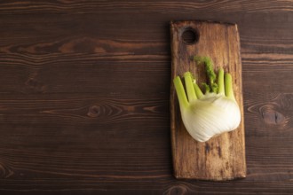 Fresh Fennel bulb on wooden cutting board on brown wooden background, top view, flat lay, copy