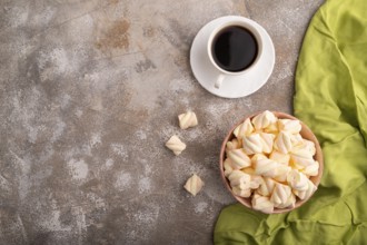 Orange and pink marshmallow in ceramic bowl on brown concrete background and green textile, top