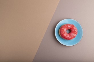 Pink Donut with sprinkles on blue ceramic plate on beige and gray pastel paper background, top