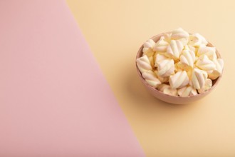 Orange and pink marshmallow in ceramic bowl on pink and orange pastel paper background, side view,