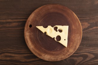 Piece of cheese with holes on cutting board on brown wooden background, top view, flat lay, copy
