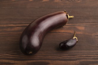 Two Eggplants big and small on brown wooden background, side view, close up, minimalism