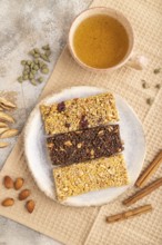 Granola bars with caramel, nuts, flakes in ceramic plate on brown concrete background, beige linen