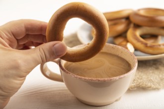 Homemade Ring Bagel with hand with cup of coffee on white wooden background and linen textile. side
