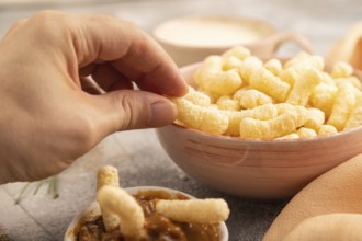 Corn flakes sticks with hand with caramel in ceramic bowl on gray concrete background and orange