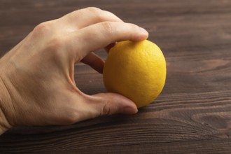 Yellow Lemon Cut in half with hand on brown wooden background. Side view, close up. healthy food,