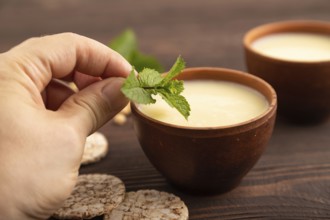 Organic non dairy banana and soy milk in clay cup with hand on brown wooden background. Vegan