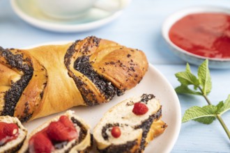 Homemade sweet bun with strawberry jam and cup of green tea on a blue wooden background. side view,